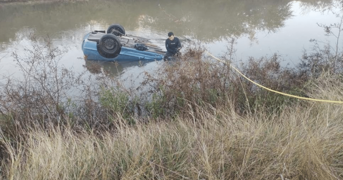 Vehículo volcado en agua con persona cerca y cuerda amarilla, relacionado con accidente en Los Mochis.
