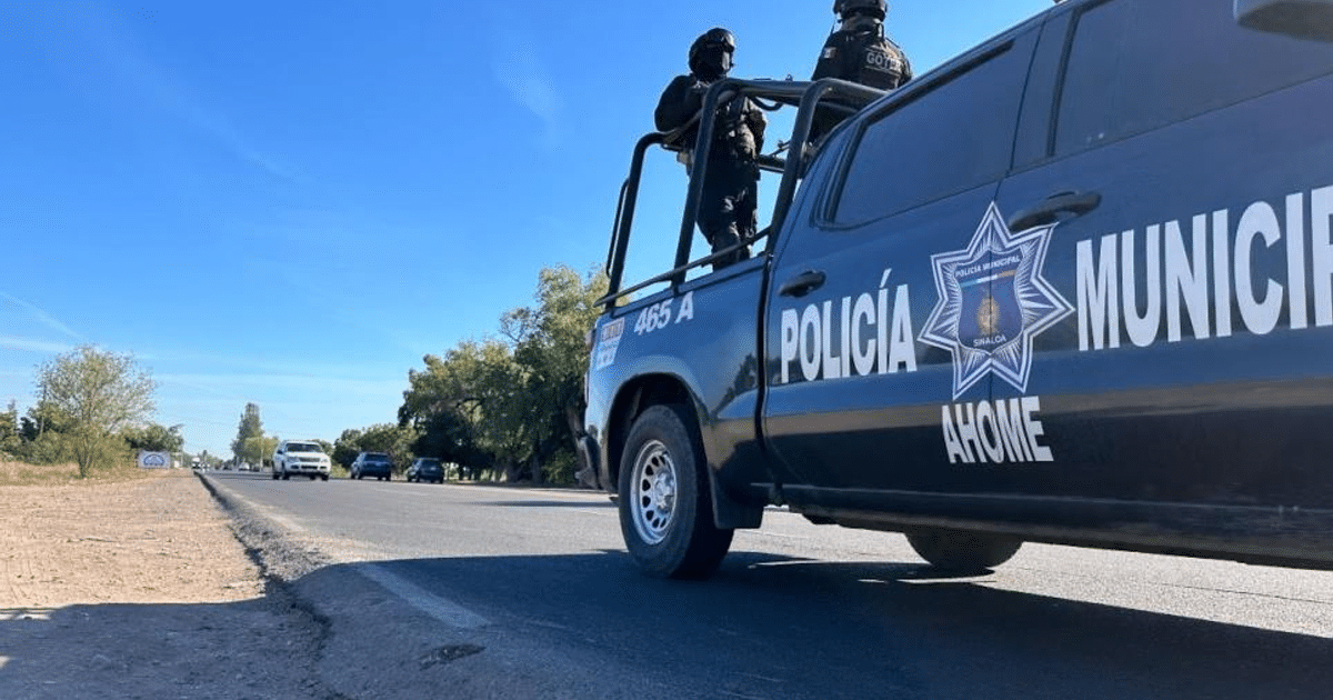Camioneta de la policía municipal de Ahome en carretera con agentes vigilando, cielo despejado y tráfico vehicular.