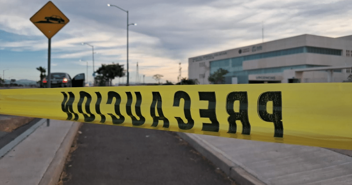 Cinta de precaución amarilla en escena urbana de Culiacán con edificio y letrero de advertencia al fondo.