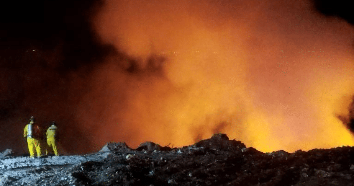 Dos personas en trajes amarillos observan un incendio en el basurón de Culiacán.