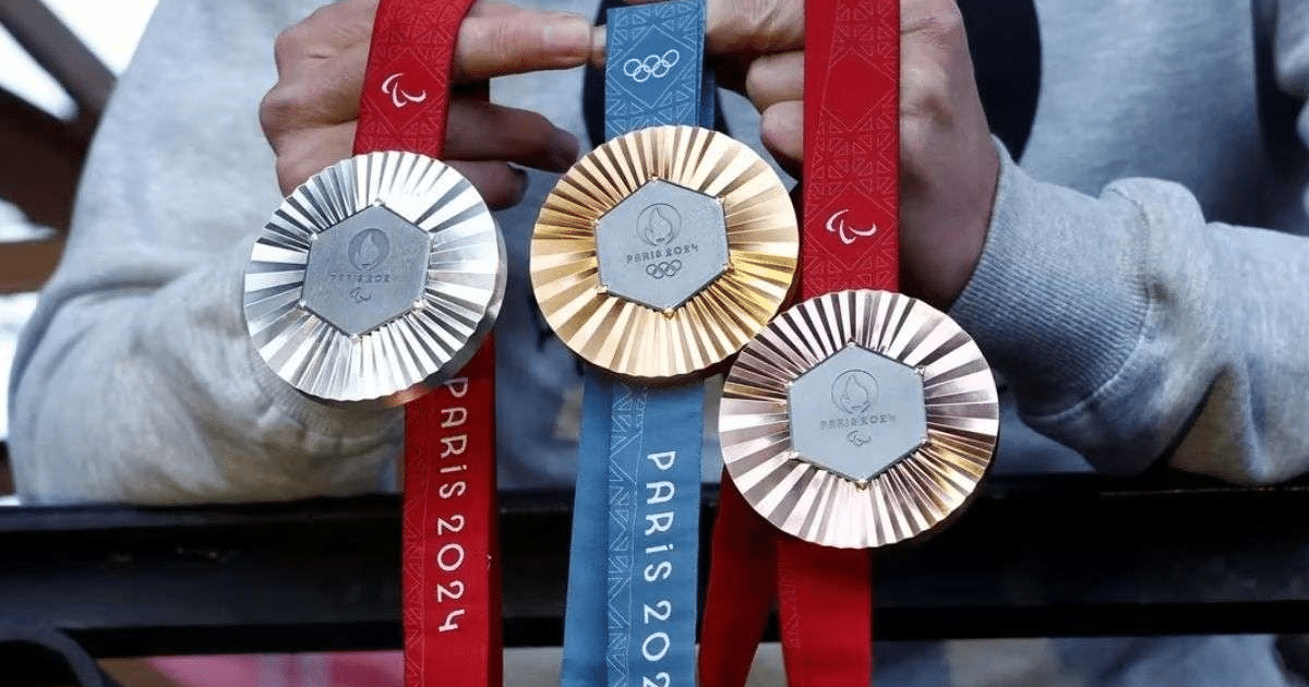 Tres medallas de los Juegos Olímpicos de París 2024 sostenidas por un atleta, con cintas de colores y símbolos olímpicos.