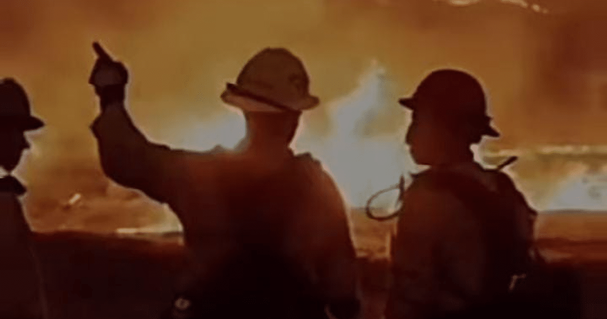 Bomberos mexicanos combatiendo un incendio en Los Ángeles, con humo y llamas visibles en el fondo.