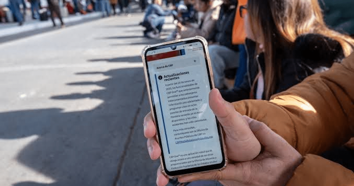 Teléfono mostrando información de CBP One con personas esperando al fondo