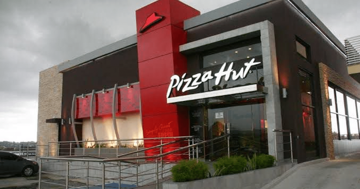 Fachada de Pizza Hut en Culiacán con letrero y automóvil estacionado, cielo nublado.