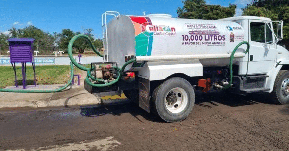 Camión cisterna de agua tratada con mangueras verdes y estructura púrpura al fondo, en un entorno al aire libre.