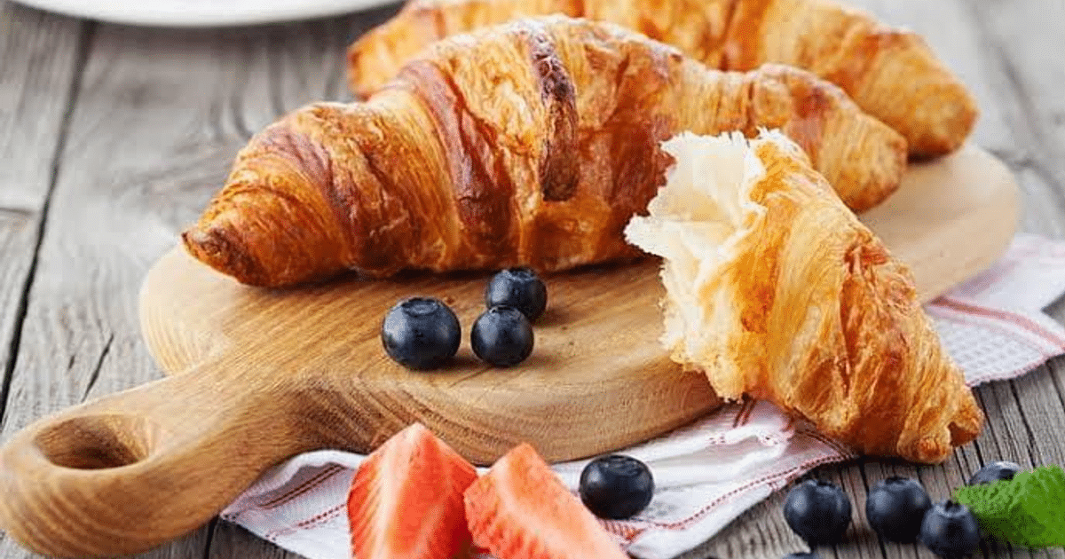 Croissants recién horneados con frutas frescas sobre una tabla de madera.