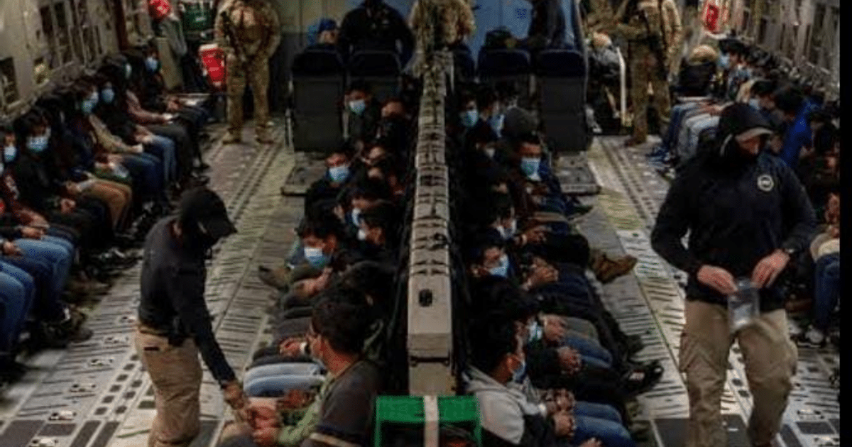 Interior de avión militar con pasajeros deportados a Guatemala, algunos con mascarillas, y una persona de pie interactuando.