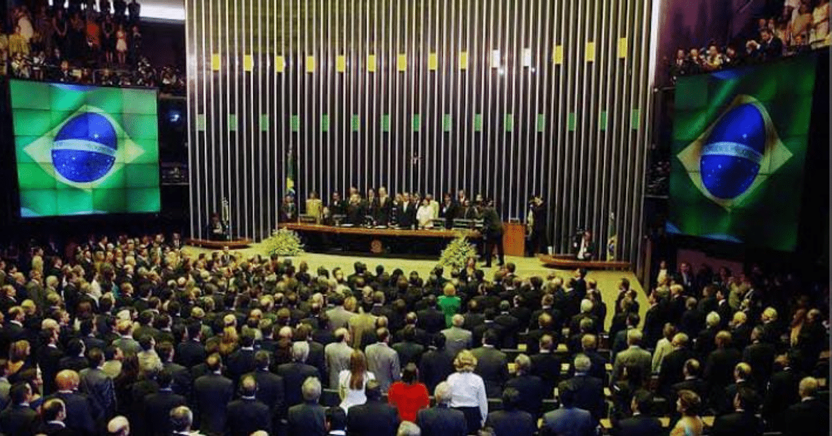 Grupo de personas en un evento legislativo en Brasil, con la bandera nacional en el fondo.