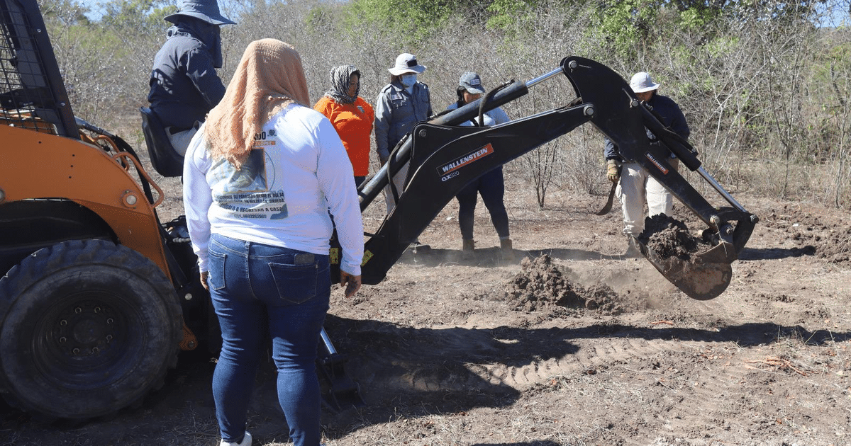 Personas trabajando con una excavadora en un terreno árido en Mazatlán, Sinaloa, durante la búsqueda de restos humanos.