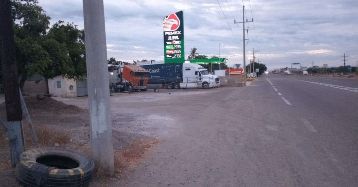 Carretera con gasolinera Pemex, camiones aparcados y entorno rural bajo cielo nublado.