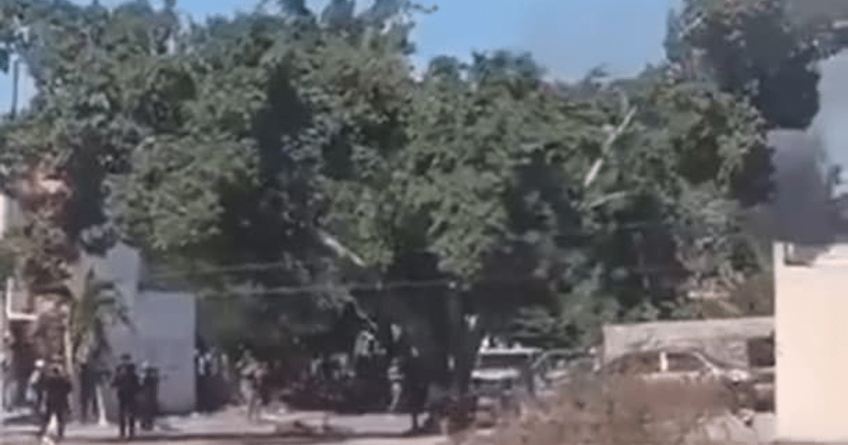 Paisaje urbano con árbol, edificios, agentes de seguridad y humo en Mazatlán tras enfrentamiento armado.