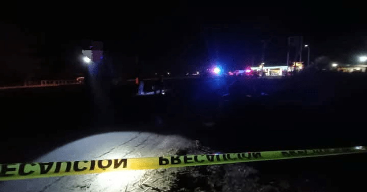 Cinta de advertencia amarilla en escena nocturna de accidente en carretera con luces de emergencia al fondo.