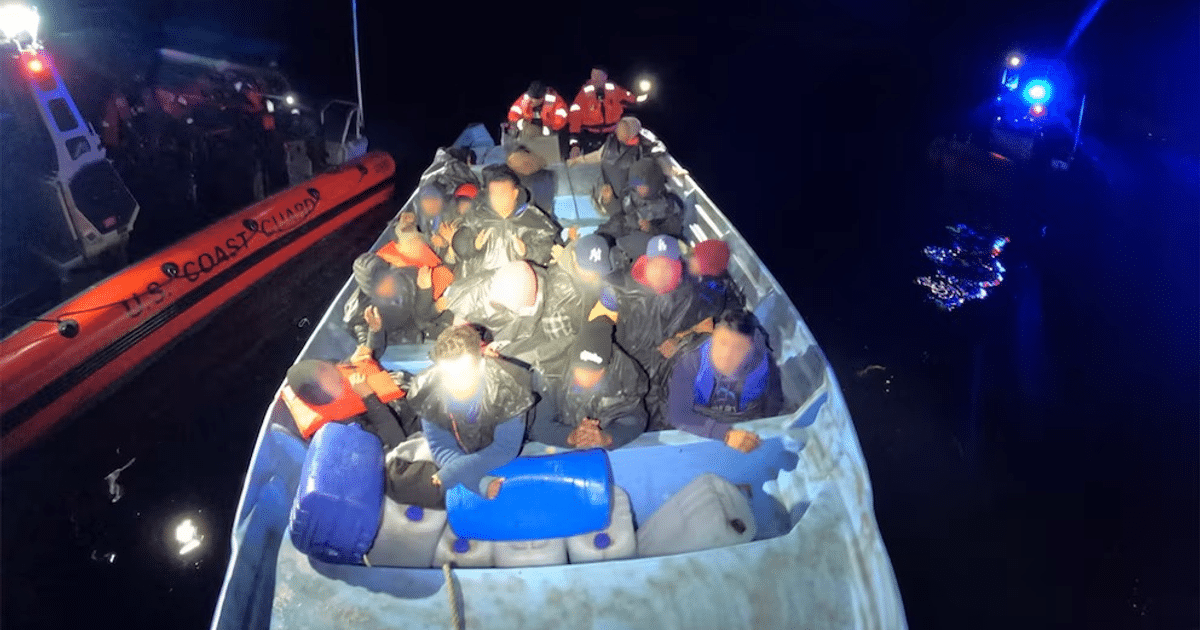 Embarcación de la Guardia Costera de EEUU interceptando un bote con migrantes en el mar nocturno.
