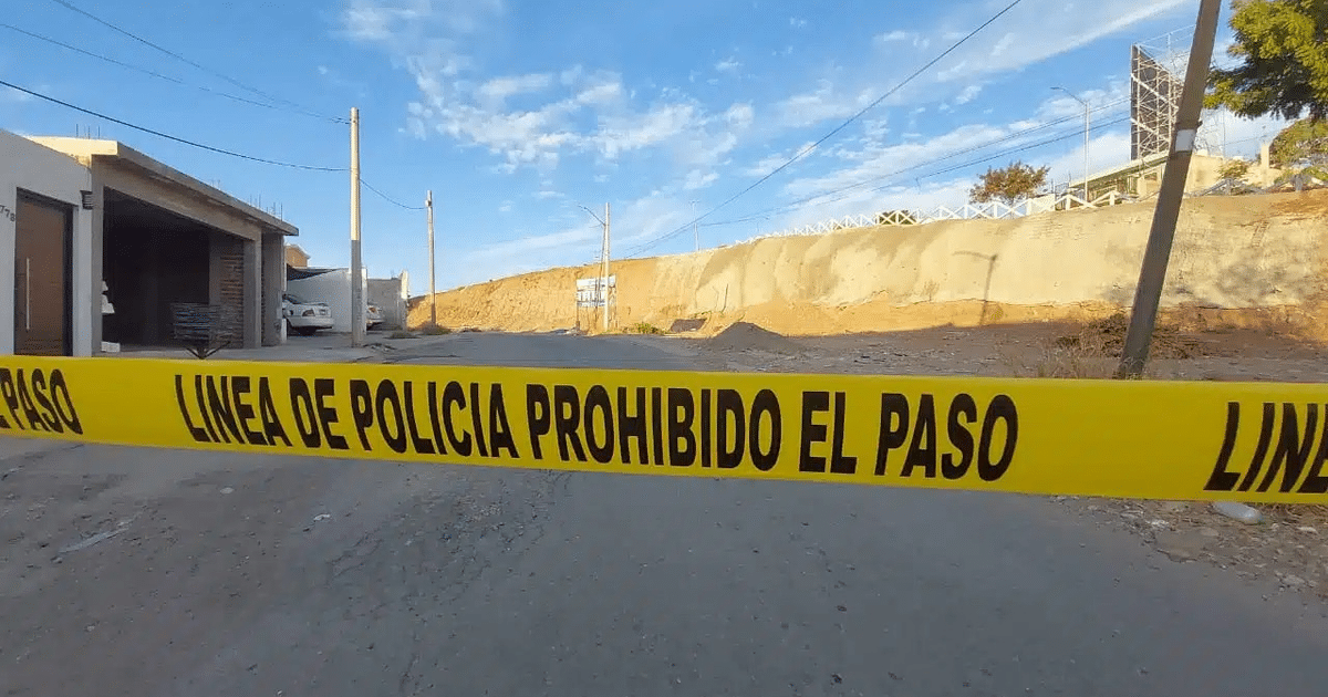Cinta amarilla de policía en escena de crimen en Culiacán, con camino y edificaciones al fondo.