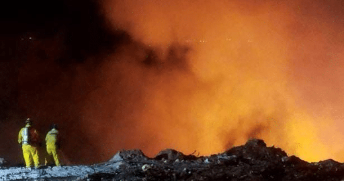 Dos personas en trajes amarillos observan un incendio nocturno con llamas naranjas en Culiacán.