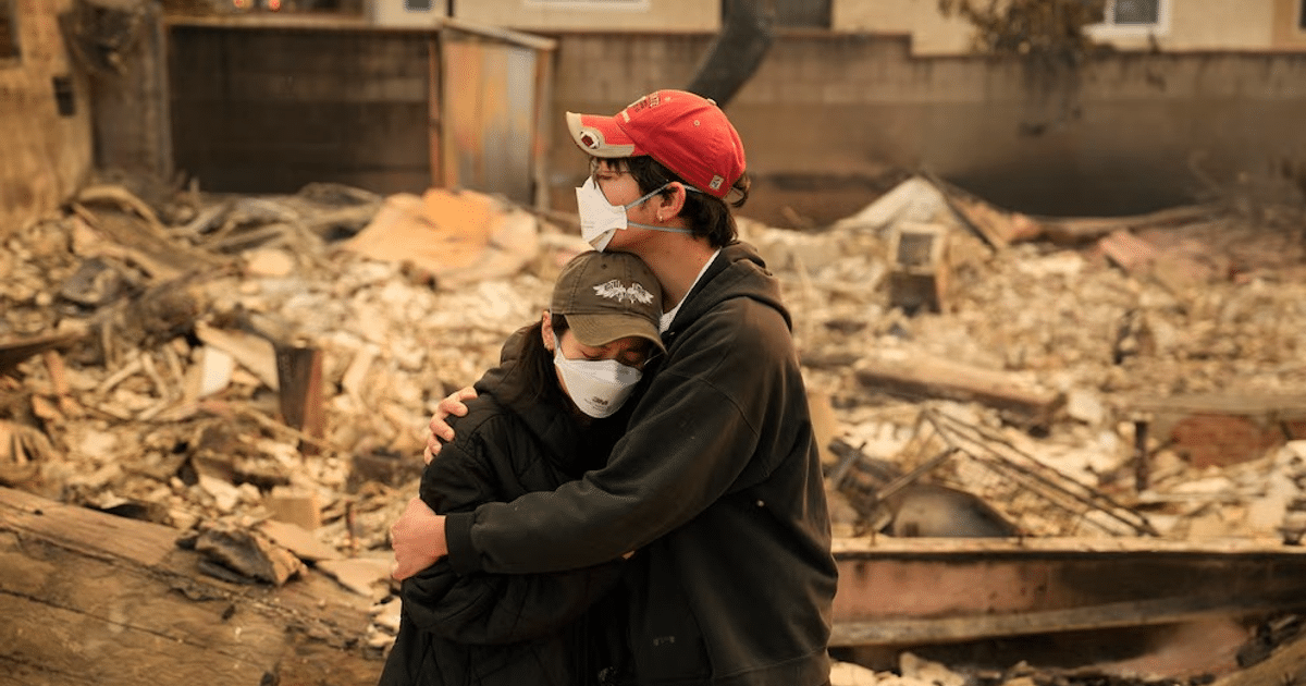 Dos personas abrazándose con mascarillas en un entorno devastado por incendios.