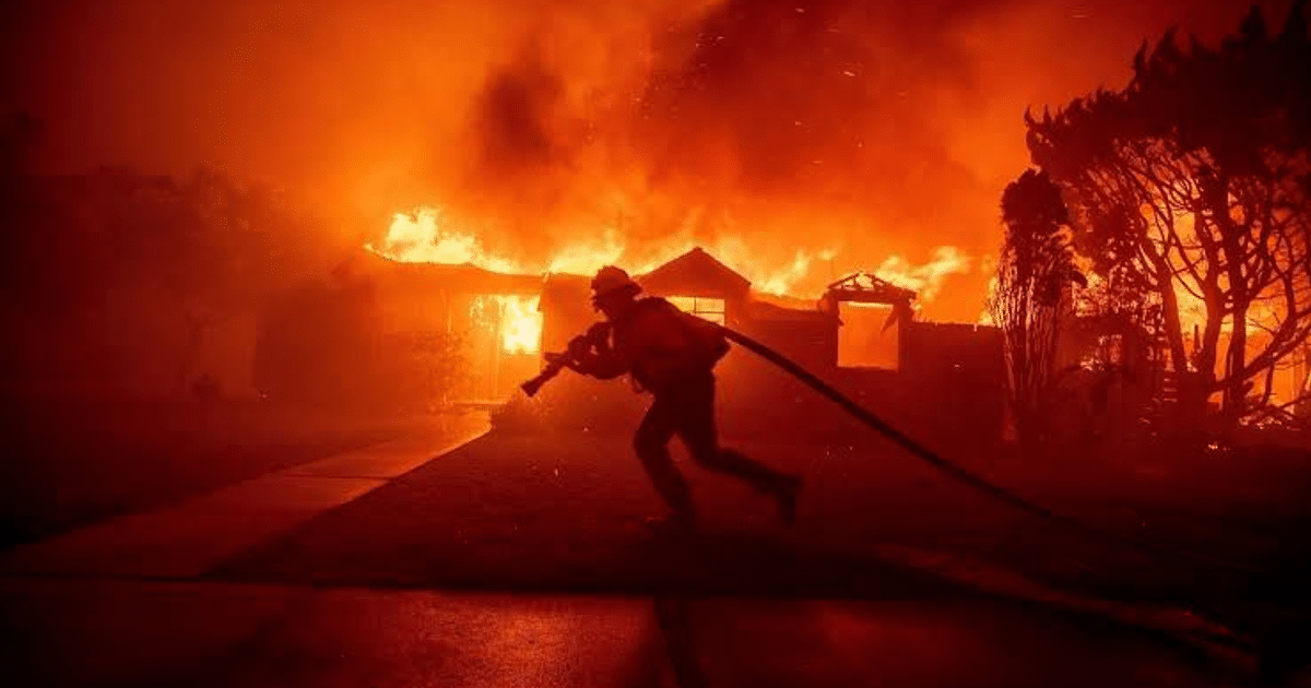 Bombero corriendo hacia un incendio urbano con llamas y humo.