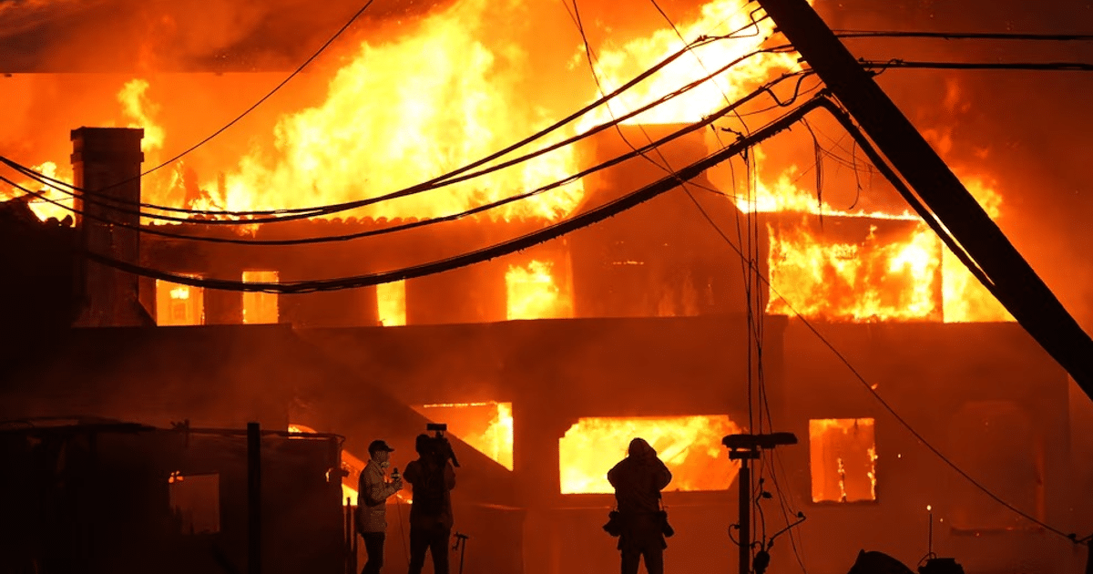 Edificio en llamas con personas en primer plano durante incendios en Los Ángeles.