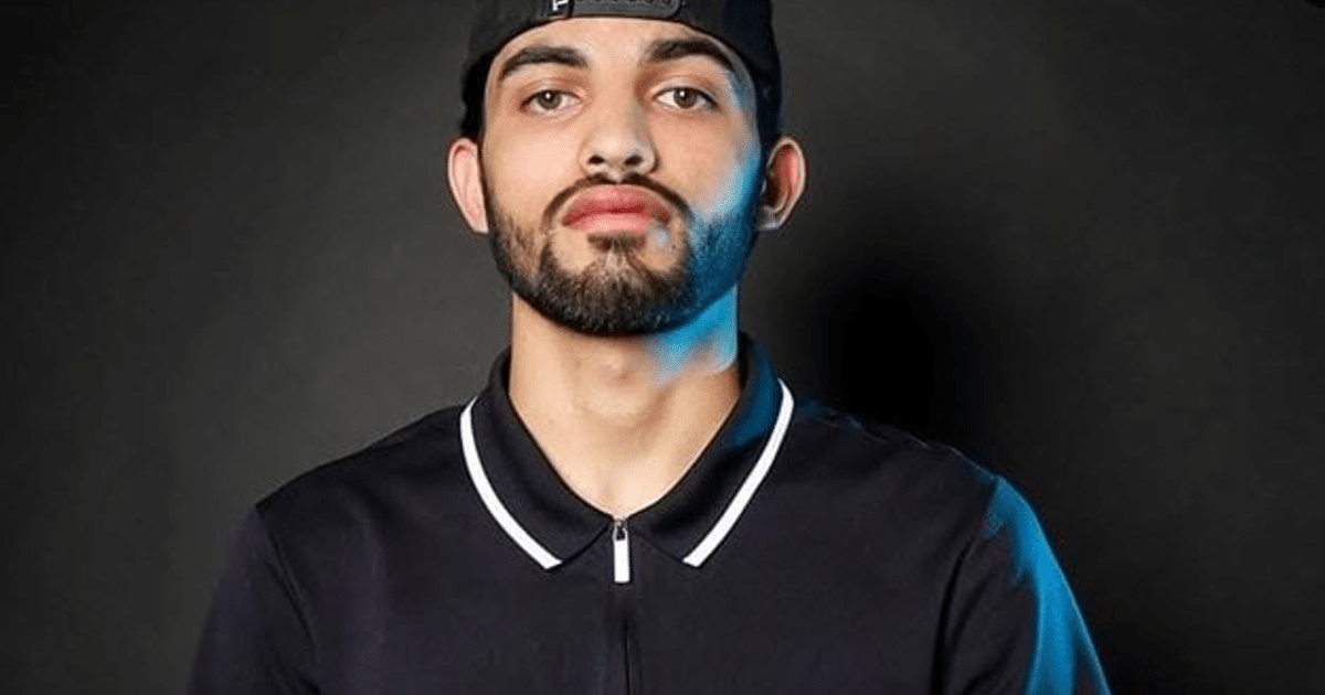 Joven con barba y gorra, camiseta negra con detalles blancos, fondo oscuro