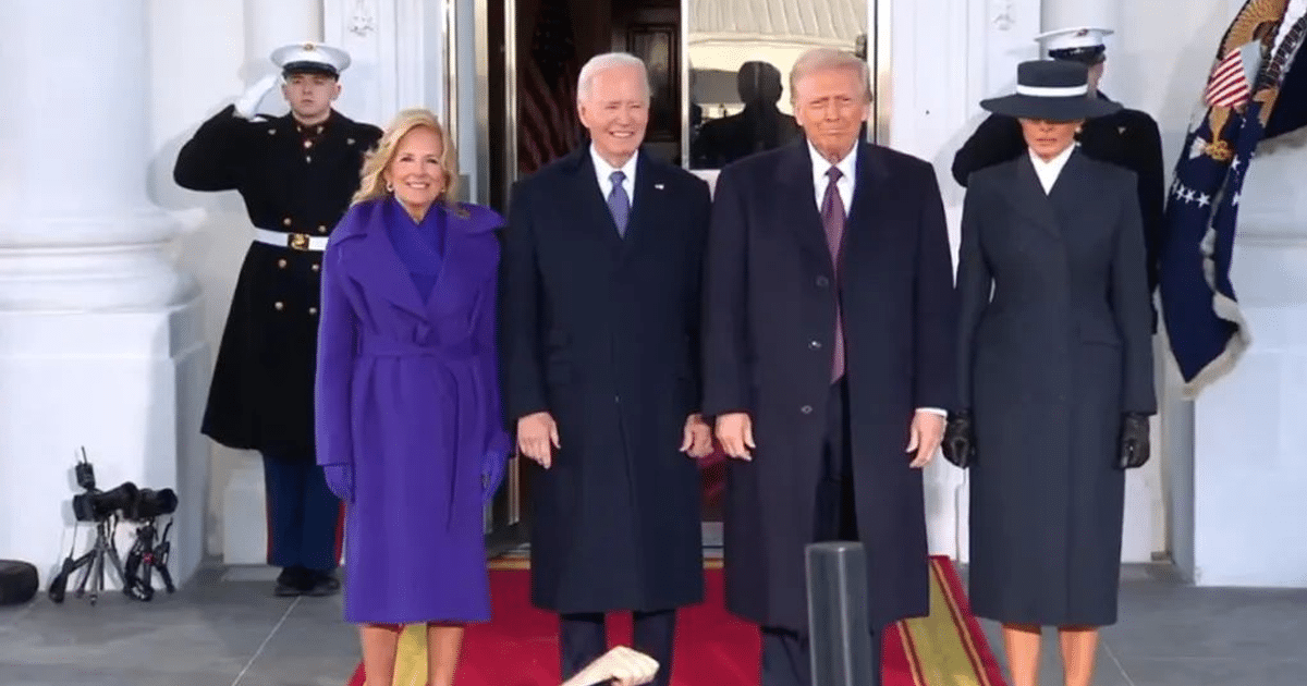 Personas en la entrada de un edificio durante la transición de poder presidencial entre Biden y Trump, con un militar saludando al fondo.