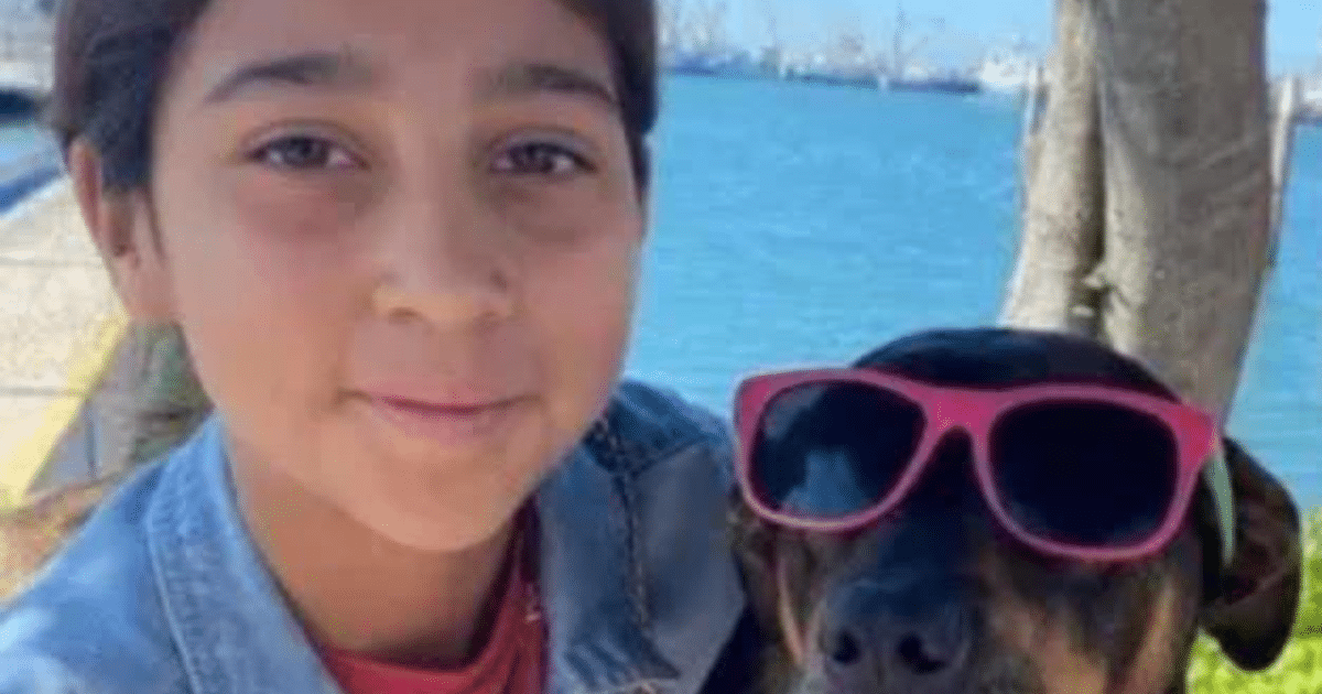 Niño sonriente con perro de gafas de sol frente a un cuerpo de agua y árboles