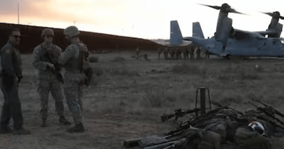 Marines y policías en un paisaje desértico al atardecer, con un helicóptero y armas en el suelo, en la frontera con México.