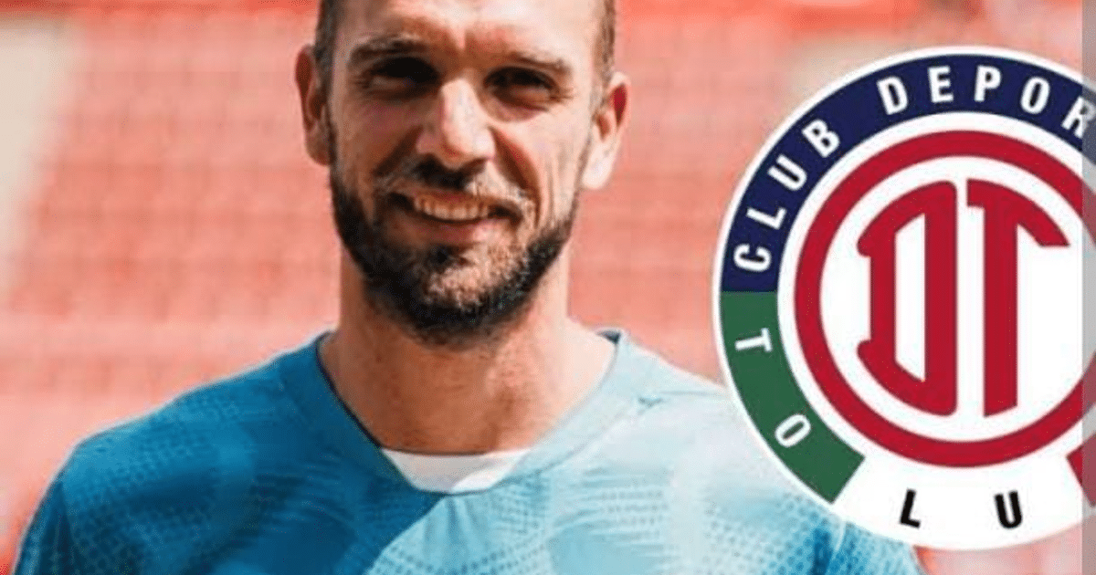 Pau López sonríe junto al escudo del Club Deportivo Toluca, vistiendo una camiseta azul.