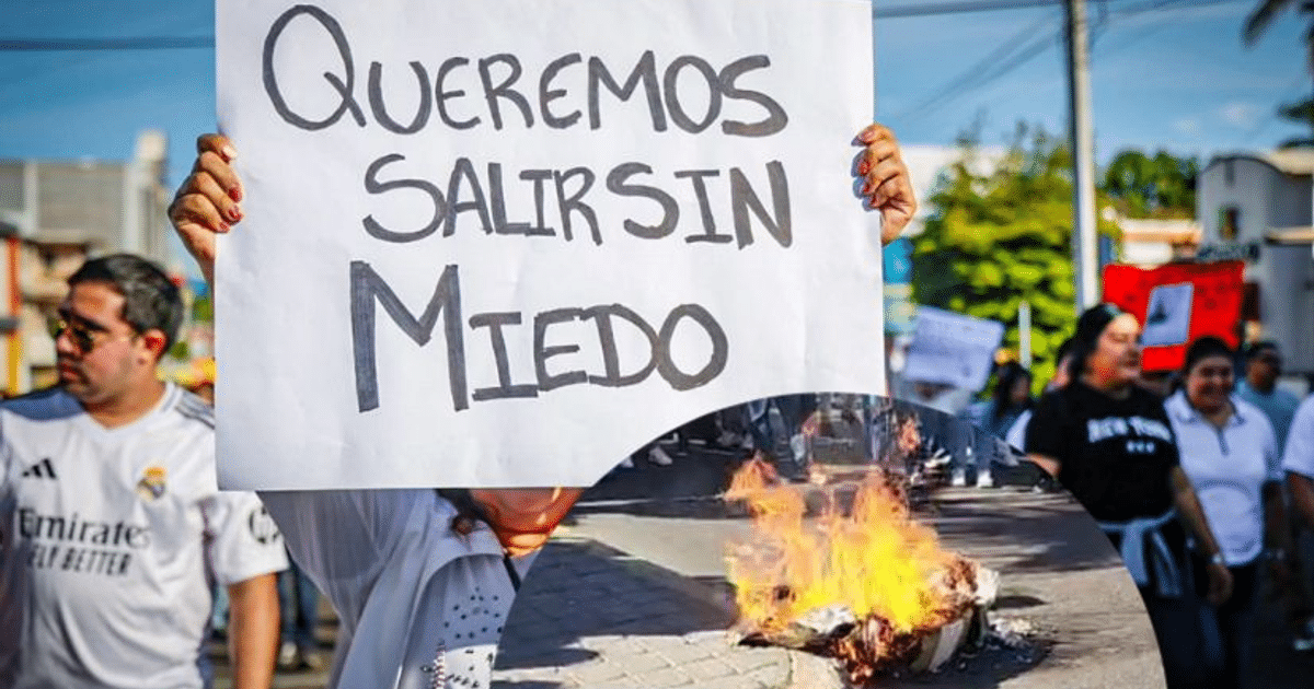 Persona sosteniendo cartel en manifestación por la paz en Culiacán, Sinaloa, con fondo de protesta y llamas.