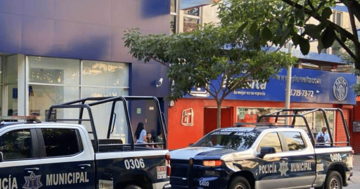 Vehículos de la policía municipal estacionados en una calle de Culiacán, con un edificio de fondo y personas cerca de la entrada.