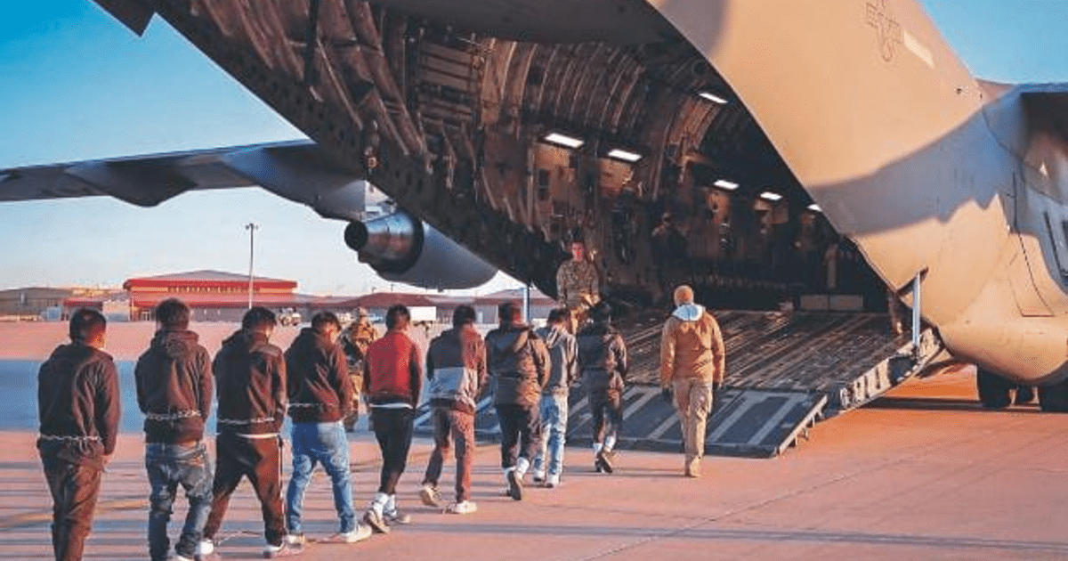 Migrantes guatemaltecos encadenados abordando un avión militar en una pista de aterrizaje, con personal militar presente.