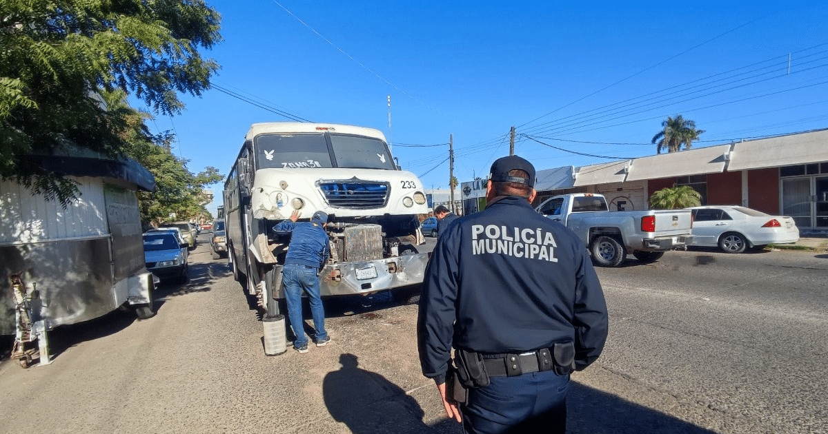 Autobús detenido con motor expuesto en Los Mochis, dos personas trabajando y policía vigilando.
