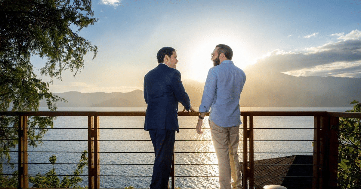 Dos hombres en un balcón contemplando un paisaje de agua y montañas, simbolizando un acuerdo migratorio.