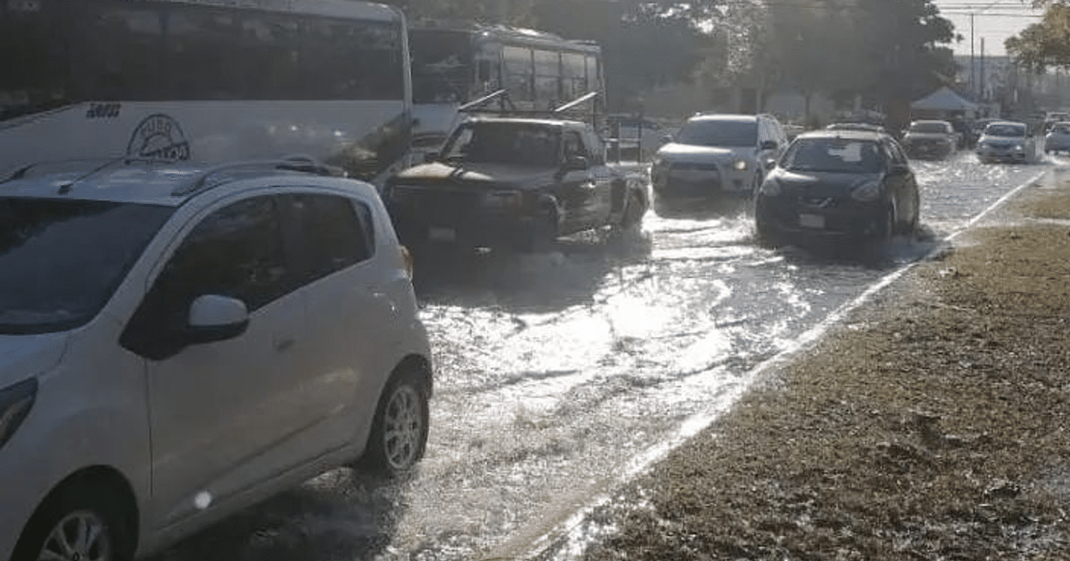 Calle inundada en Mazatlán con vehículos parcialmente sumergidos, incluyendo un autobús y coches.