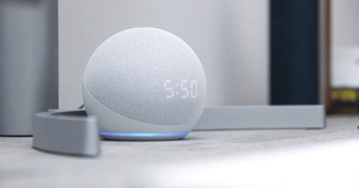 Altavoz inteligente blanco con pantalla mostrando la hora, junto a un objeto gris tubular en un entorno minimalista.