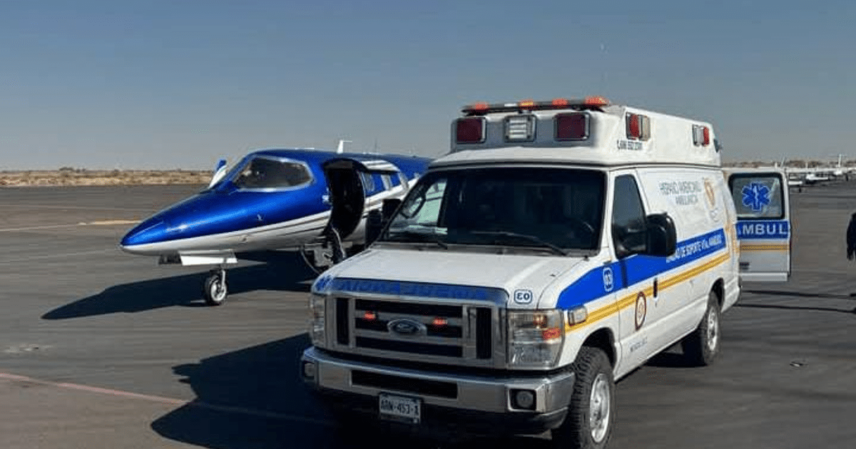 Avión azul y blanco estacionado junto a una ambulancia de emergencia en un aeródromo.