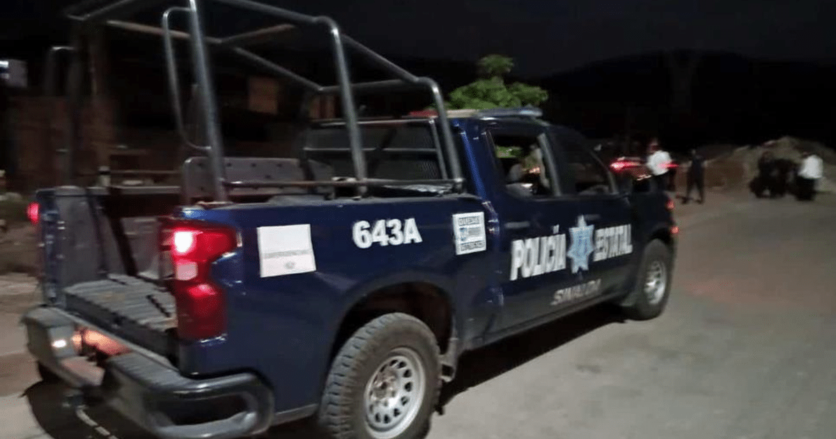 Camioneta de policía azul en Culiacán durante la noche, con personas y escombros en el fondo.