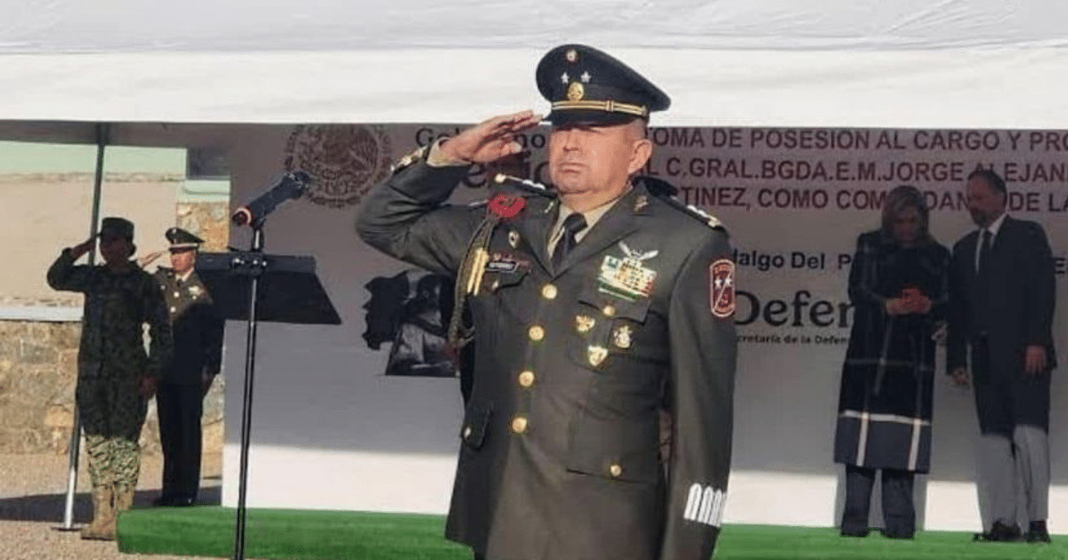 Militar saludando en ceremonia oficial de relevos, con fondo de uniformados y micrófono.