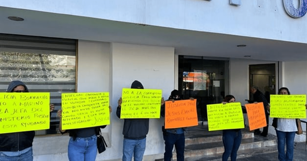 Manifestantes con carteles amarillos y naranjas exigiendo justicia frente a un edificio.