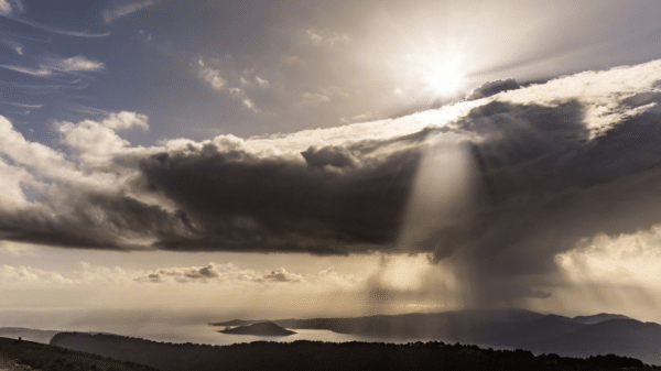 Paisaje natural con cielo nublado, rayos de sol, montañas y agua en el horizonte