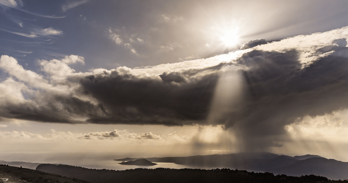 Paisaje natural con cielo nublado, rayos de sol, montañas y agua en el horizonte