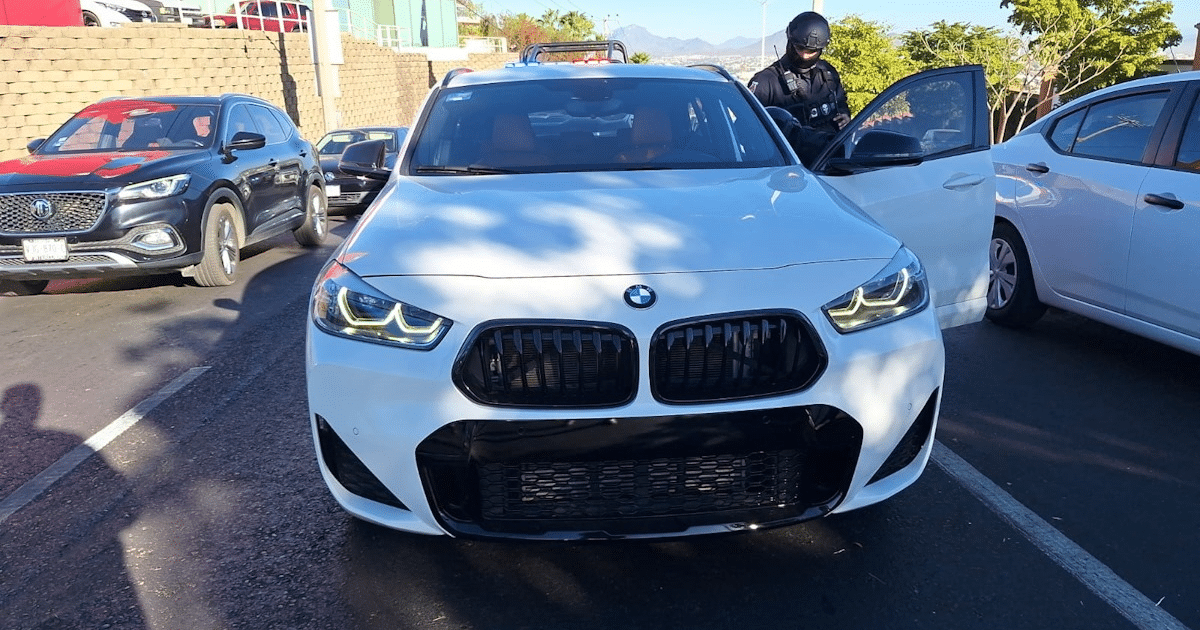 BMW blanco detenido en carretera con oficial de seguridad al lado, relacionado con un robo en Culiacán.