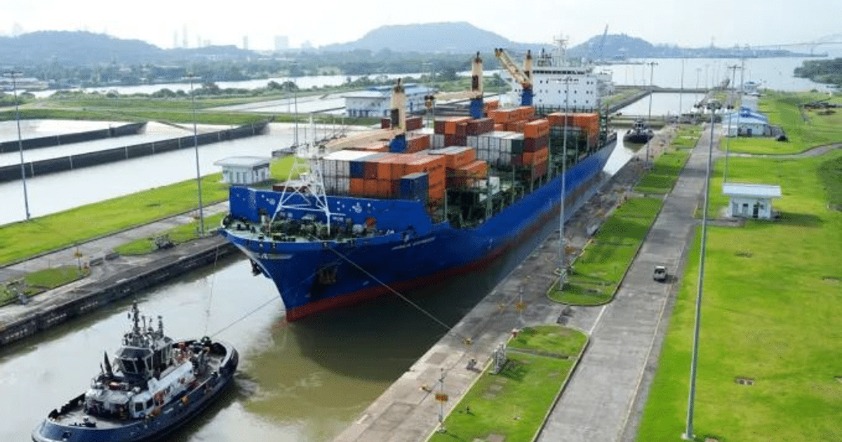 Barco de carga en el Canal de Panamá con remolcador y paisaje montañoso al fondo.
