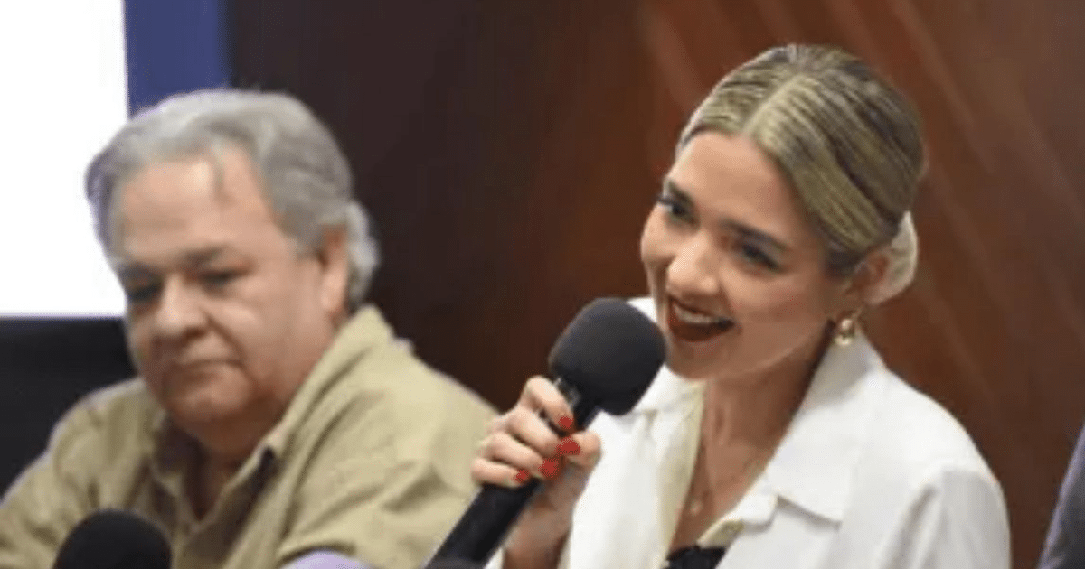 Dos personas en una conferencia sobre el Carnaval Mazatlán 2025, una hablando con micrófono y otra escuchando.