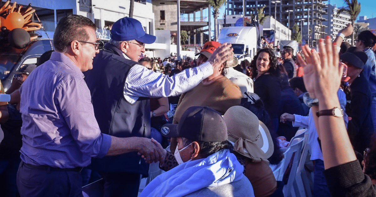 Personas interactuando y celebrando en el Carnaval de Mazatlán, con un fondo urbano y multitud.