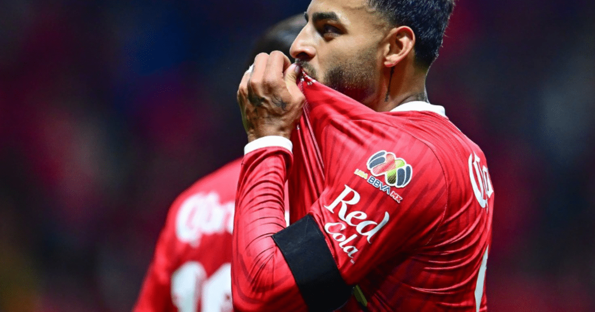 Jugador de fútbol con camiseta roja besando el escudo en el estadio Nemesio Diez