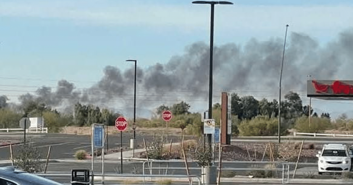 Humo negro en el horizonte tras accidente aéreo en Arizona, con señales de alto y elementos urbanos en primer plano.