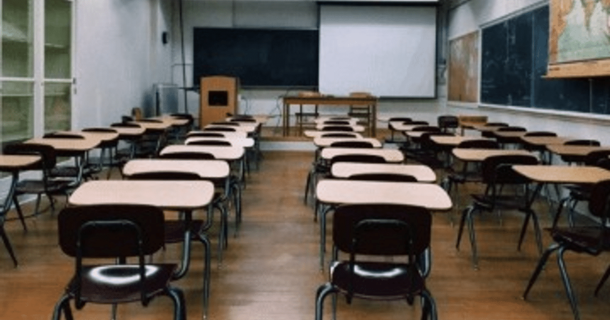 Aula vacía con escritorios y sillas, pizarra y pantalla al fondo, lista para clases virtuales en Culiacán.