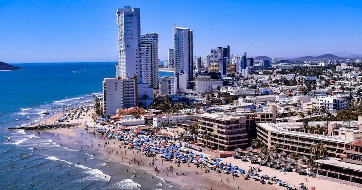 Playa en Mazatlán con edificios altos y sombrillas, en un día de clima frío.