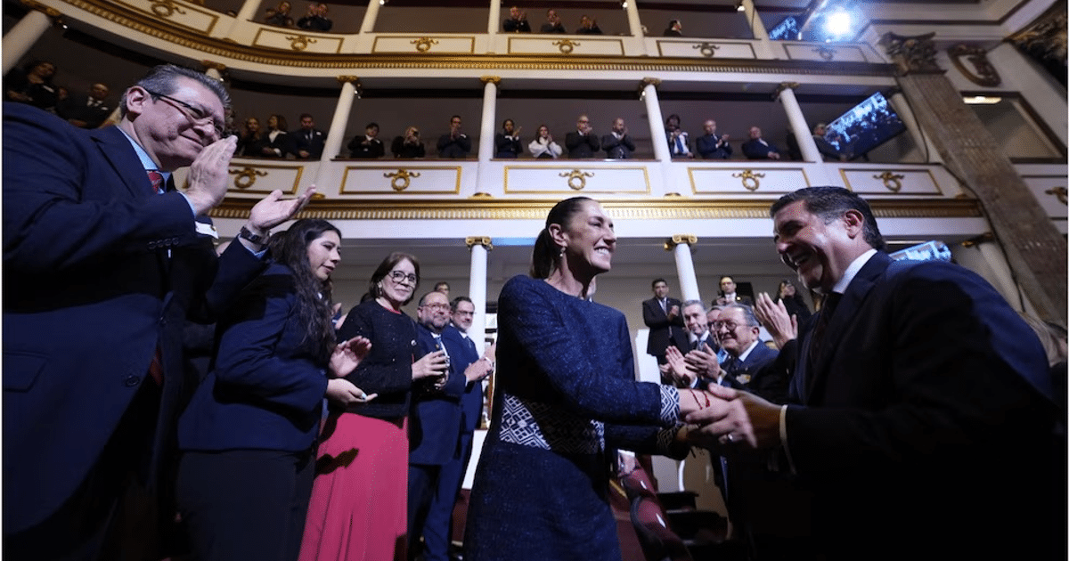 Personas aplaudiendo en un auditorio durante un evento formal, con una mujer sonriendo y estrechando la mano de un hombre.