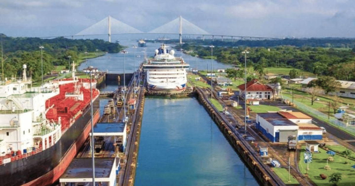 Barcos navegando en el Canal de Panamá con un puente al fondo, rodeados de vegetación y edificios.